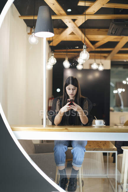 Piena lunghezza di fiduciosa giovane donna utilizzando il telefono cellulare mentre seduto in mensa illuminata — Foto stock