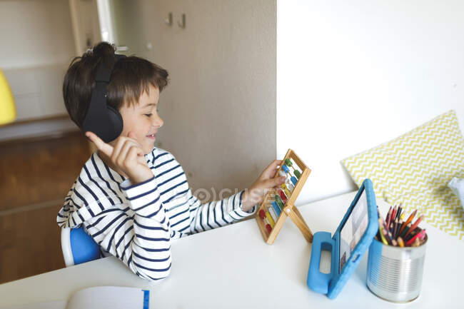 Junge macht Hausaufgaben und benutzt Rechenschieber, Tablet und Kopfhörer zu Hause — Stockfoto