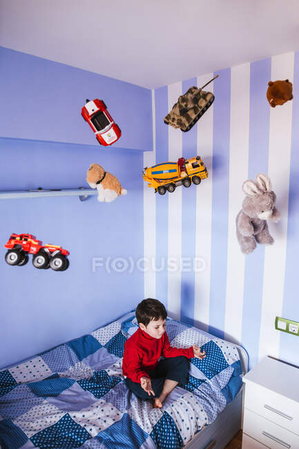 Pequeño niño meditando en su cama con juguetes volando sobre su cabeza - foto de stock