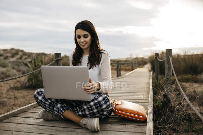 Woman sitting on a boardwalk in the countryside using laptop — Stock Photo