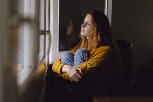 Donna dai capelli rossi pensieroso seduto alla finestra aperta guardando la distanza — Foto stock