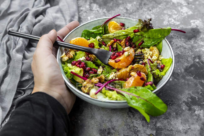 Hand holding bowl of winter salad with lettuce, tangerines, walnuts, feta and pomegranate seeds — Stock Photo