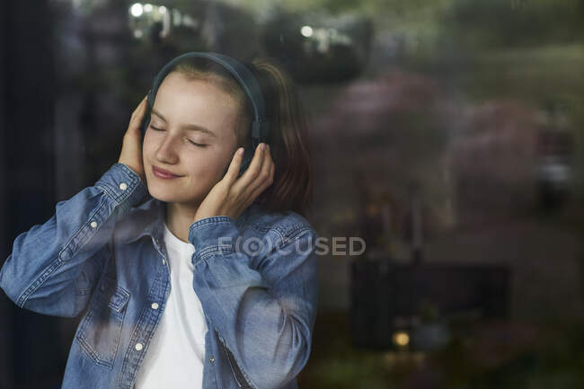 Pre-adolescent girl with eyes closed enjoying music listening through headphones at home — Stock Photo