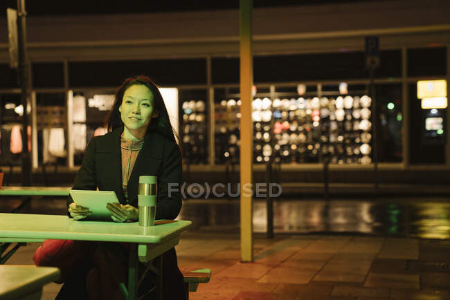 Young woman using tablet on a coffee shop terrace in the city at night, Frankfurt, Germany — Stock Photo