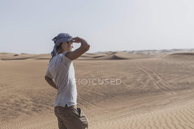 Homem turista blindagem olhos enquanto em pé em dunas de areia no deserto em Dubai, Emirados Árabes Unidos — Fotografia de Stock