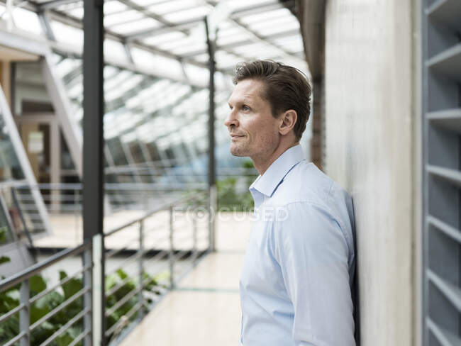 Businessman in green atrium., leaning on wall — Stock Photo