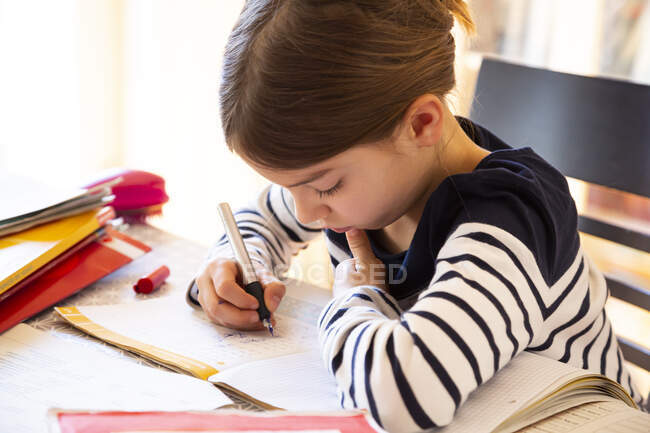 Girl doing homework while sitting at table in room — Stock Photo