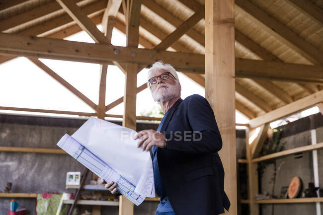 Старший з будівельним планом стоїть у сховищі і дивиться вгору. — стокове фото