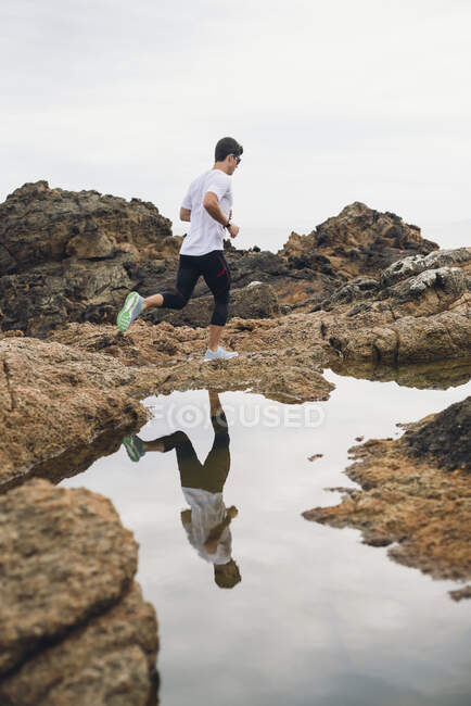 Lungo tutto il percorso maschile corridore su rocce durante la corsa dalla sua riflessione sull'acqua sulla costa, Ferrol, Galizia, Spagna — Foto stock