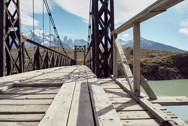 Puente de hierro y madera sobre el agua y montañas Torres del Paine al fondo, Parque Nacional Torres del Paine, Chile - foto de stock