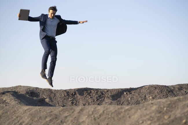 Reifer Geschäftsmann mit Laptop springt auf eine ausgediente Minenspitze — Stockfoto