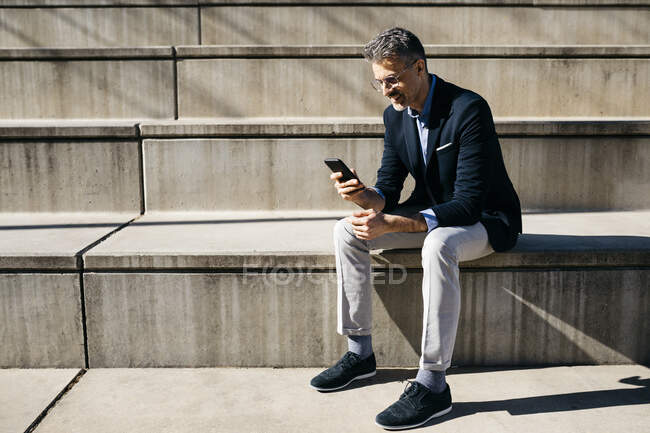 Homme d'affaires aux cheveux gris assis dans un escalier à l'aide d'un téléphone portable — Photo de stock