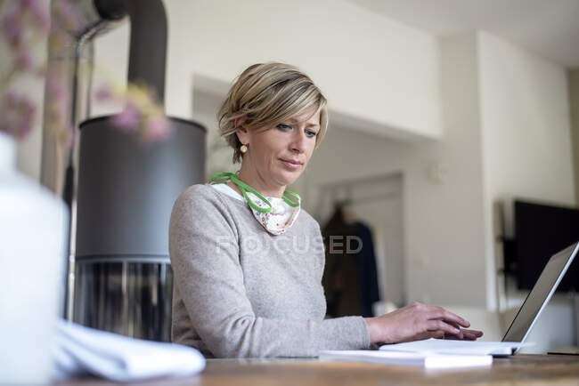 Femme mature travaillant à la maison tout en utilisant un ordinateur portable dans le salon — Photo de stock