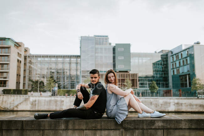 Young couple sitting on a wall at the riverbank, Berlin, Germany — Stock Photo