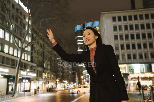 Young woman hailing a taxi in the city at night, Frankfurt, Germany — Stock Photo