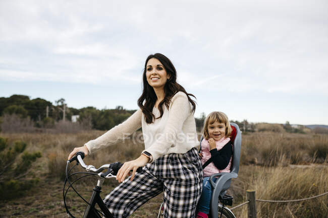 Donna in bicicletta in campagna con figlia nel seggiolino per bambini — Foto stock