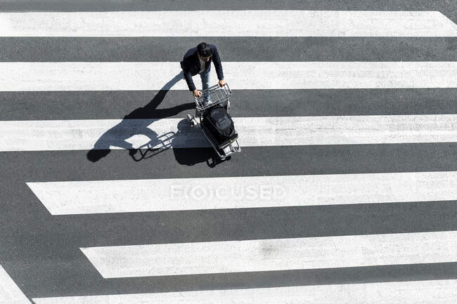 Uomo sulla zebra che attraversa spingendo carrello bagagli, vista dall'alto — Foto stock