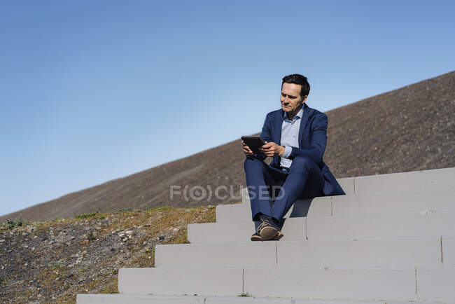 Reifer Geschäftsmann sitzt auf einer Treppe auf einer stillgelegten Minenspitze mit Tablette — Stockfoto