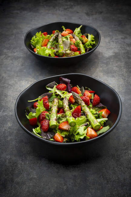Two bowls of vegetarian salad with lettuce, strawberries and asparagus — Stock Photo