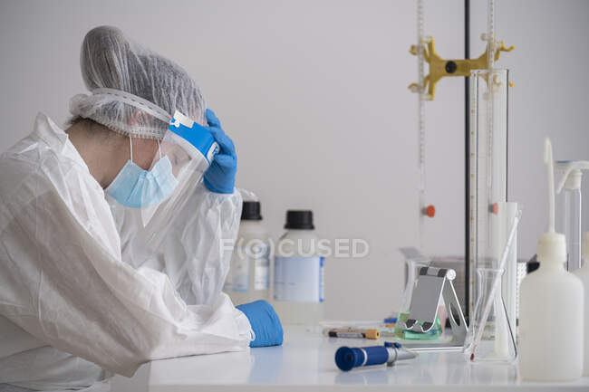 Уставший ученый в защитной одежде сидит за столом — стоковое фото
