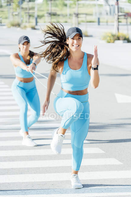 Young twin sisters exercising with resistance band on sunny day — Stock Photo