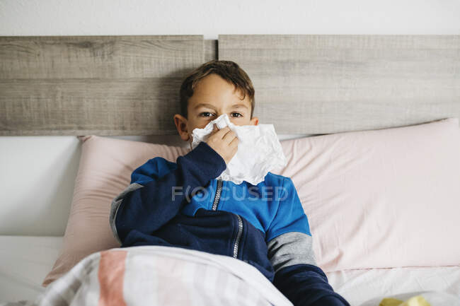 Retrato del niño enfermo acostado en la cama sonándose la nariz - foto de stock