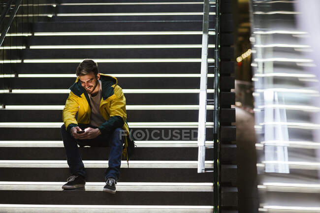 Усміхнений чоловік сидить на сходах на станції метро за допомогою мобільного телефону — стокове фото