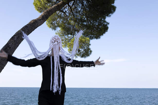 Woman wearing crocheted white headdress with fringes standing in front of the sea moving — Stock Photo