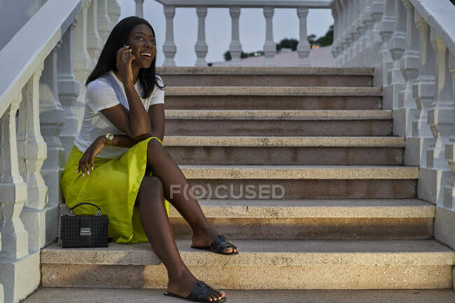 Ritratto di giovane donna sorridente al telefono seduta sulle scale all'aperto — Foto stock