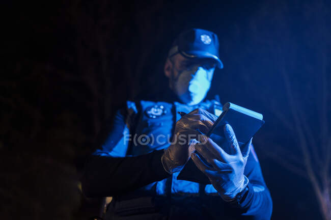 Policier pendant une mission d'urgence la nuit, prenant des notes, portant des gants de protection et un masque — Photo de stock