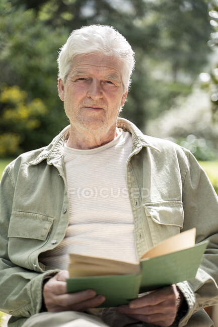 Портрет старшого чоловіка, який читає книжку, сидячи на подвір 