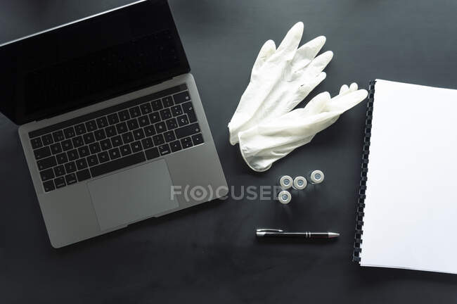 Directly above shot of medical samples with gloves and spiral notebook by laptop on table — Stock Photo
