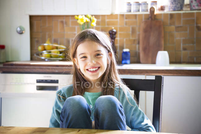 Smiling girl sitting at kitchen table and looking at camera — Stock Photo