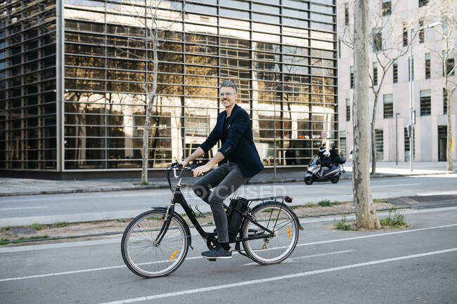 Homme d'affaires aux cheveux gris en vélo électrique à travers le centre-ville — Photo de stock