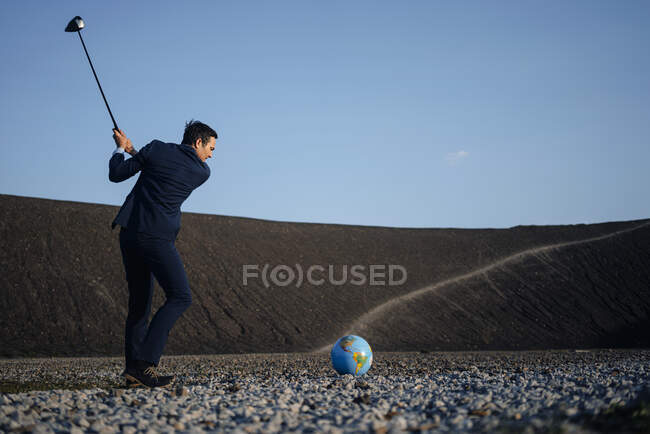 Mature businessman playing golf with a globe on a disused mine tip — Stock Photo