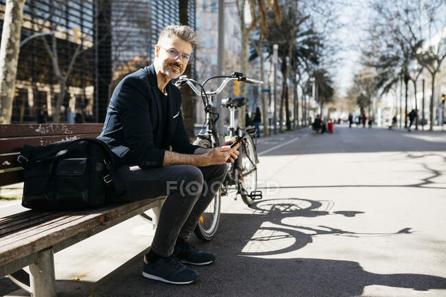 Ritratto di uomo d'affari dai capelli grigi seduto su una panchina accanto alla bicicletta in città — Foto stock