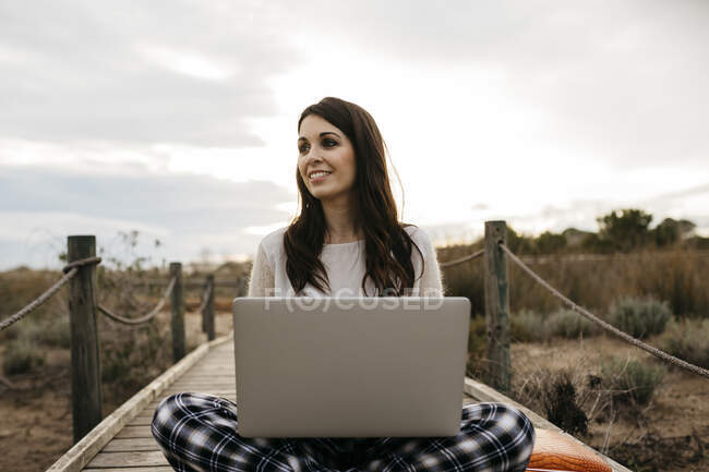Жінка сидить на набережній у сільській місцевості з ноутбуком. — стокове фото