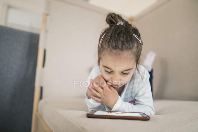 Маленька дівчинка лежить і дивиться на смартфон. — стокове фото