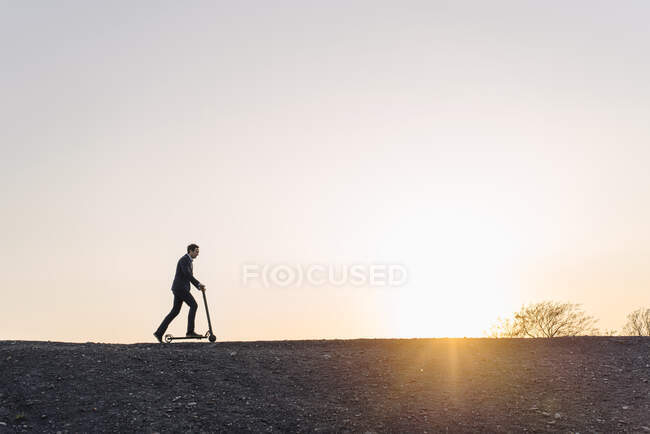 Homme d'affaires mature avec un scooter de coup de pied sur une pointe de mine désaffectée au coucher du soleil — Photo de stock