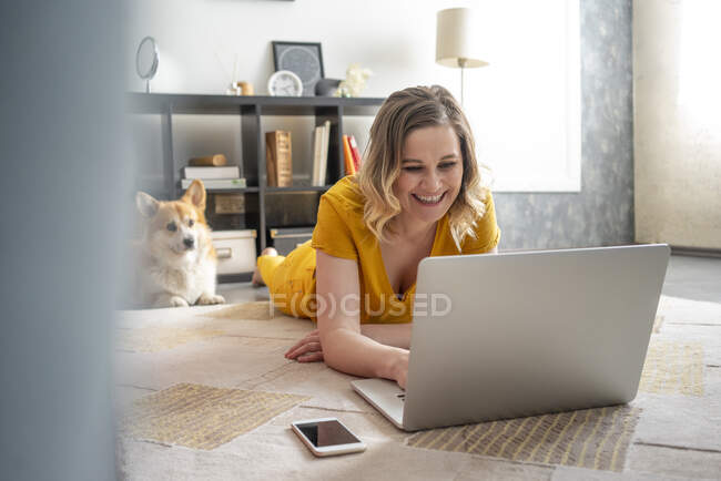 Mulher feliz com cão usando laptop na sala de estar em casa — Fotografia de Stock