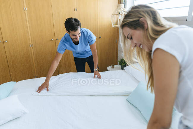 Sorridente coppia organizzare letto insieme in camera da letto a casa — Foto stock