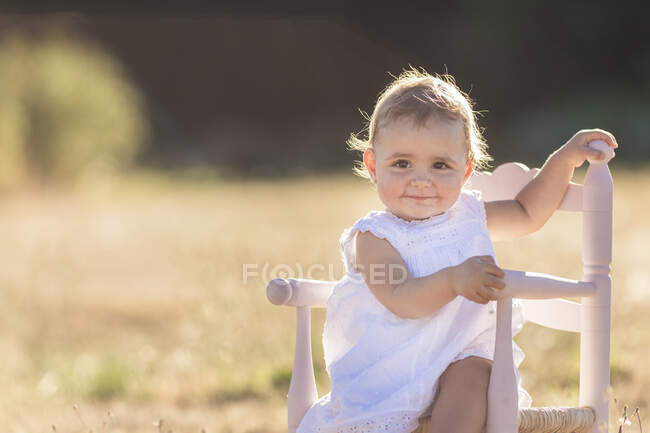 Retrato de linda chica sentada en la silla en el prado durante el día soleado - foto de stock