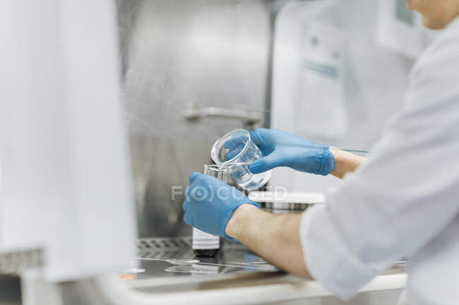 Молодий чоловік - технік виливає хімічні речовини з пекарні під час дослідження в лабораторії. — стокове фото