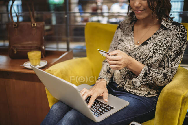 Gros plan d'une jeune femme assise dans un fauteuil avec un ordinateur portable et une carte de crédit — Photo de stock