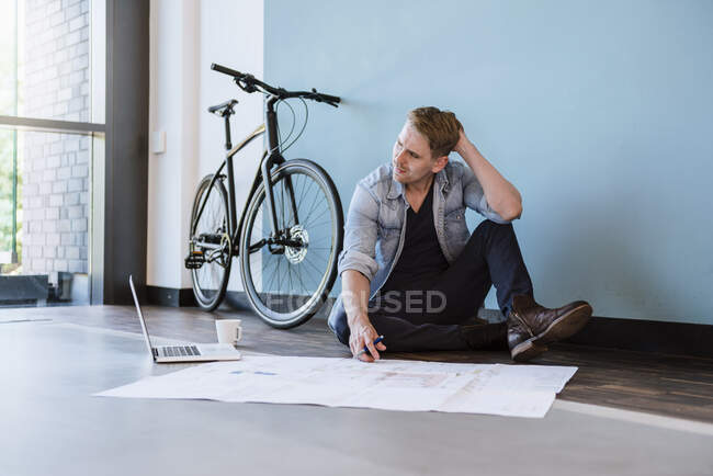 Hombre de negocios casual sentado en el piso de la oficina del loft, trabajando en un plano - foto de stock
