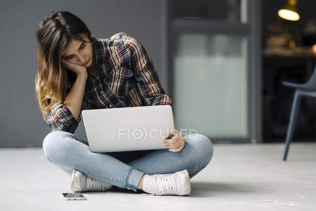 Pensive young freelancer sitting on the floor looking at laptop — Stock Photo