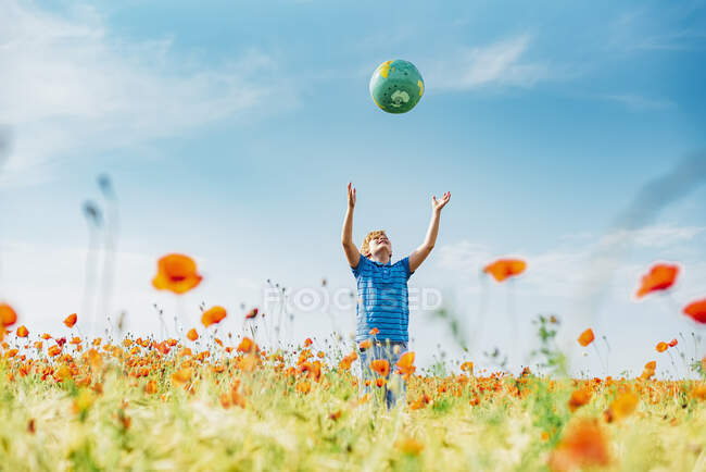 Мальчик ловит глобус, стоя в маковом поле на фоне голубого неба в солнечный день — стоковое фото