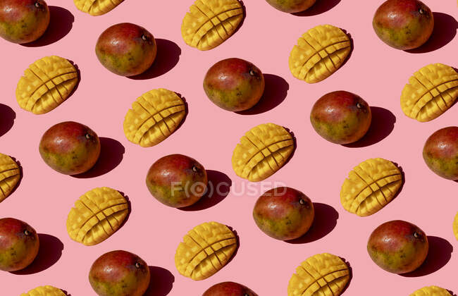 Patrón de mango entero y picado sobre fondo rosa - foto de stock