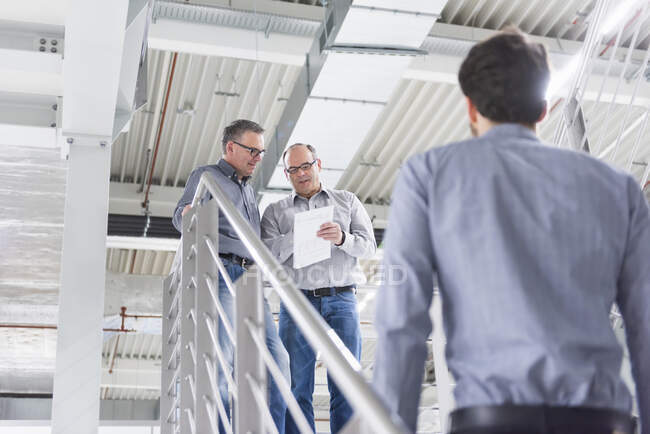 Tres hombres de negocios discutiendo en una fábrica - foto de stock