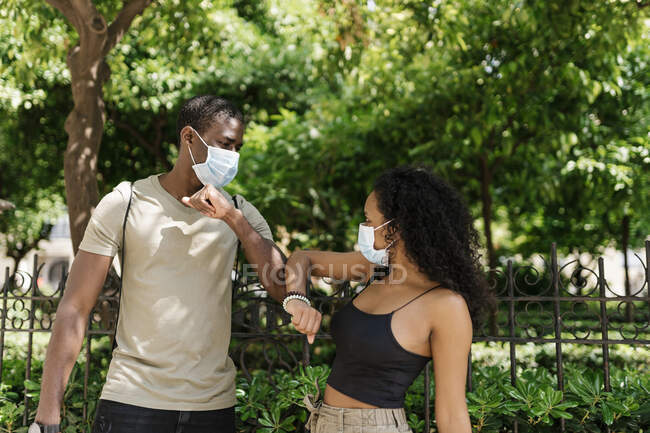 Чоловік і жінка у масках вітаються, торкаючись ліктів у парку. — стокове фото